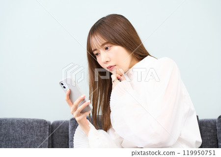 Young woman in plain clothes, living room, smartphone 119950751