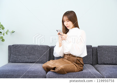 Young woman in plain clothes, living room, smartphone 119950758