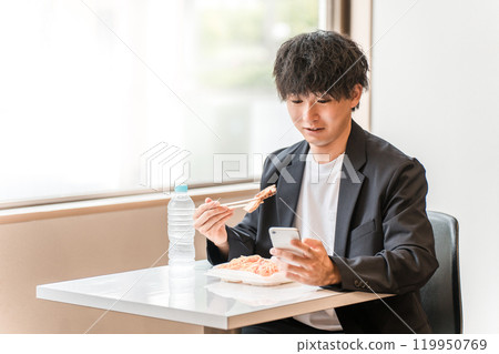 A young Asian male businessman eating lunch while looking at his smartphone in the eat-in space 119950769