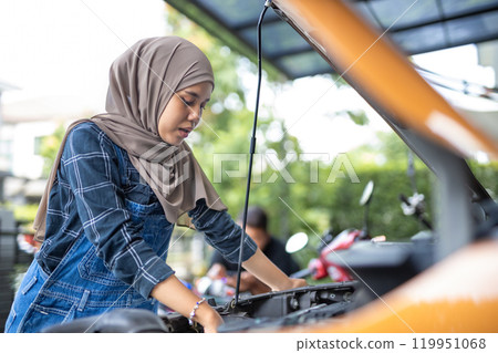 Asian muslim wear hijab woman checking up automobile engine before departure. Female trying fix their car to motor mechanic. 119951068