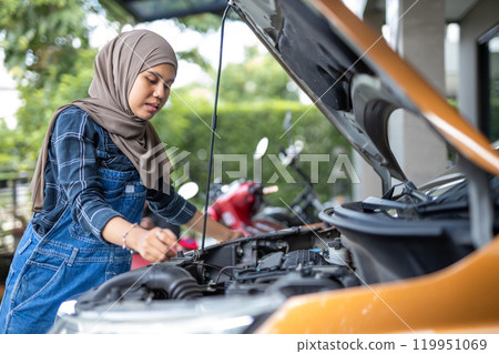 Asian muslim wear hijab woman checking up automobile engine before departure. Female trying fix their car to motor mechanic. Asian muslim wear hijab woman checking up automobile engine before departure. Female trying fix their car to motor mechanic. 119951069