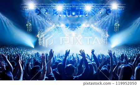 The backs of a large audience gathered at an outdoor concert venue illuminated by lights at night 119952050