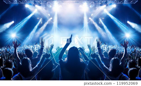 The backs of a large audience gathered at an outdoor concert venue illuminated by lights at night 119952069