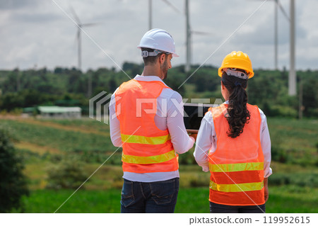 Team engineer wearing safety uniform holding laptop discussed plan about renewable energy at station energy power wind. technology protect environment reduce global warming problems. 119952615