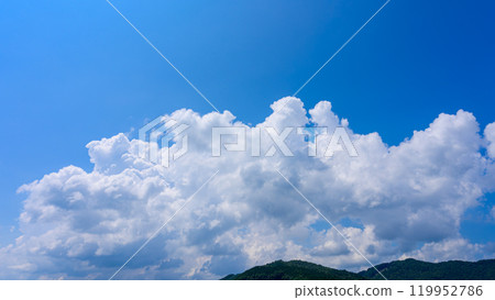 Under the blue summer sky, many white clouds float over the mountaintops 119952786