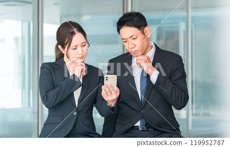 Businessman and businesswoman talking while looking at smartphones/smartphones (video/app/search/news) 119952787