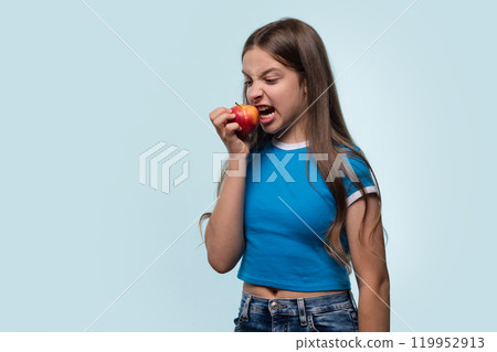 Young girl bites into red apple with playful expression. 119952913