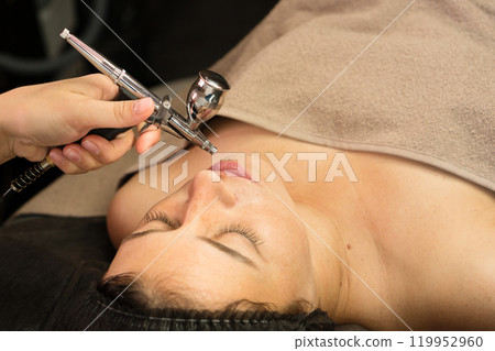 Aesthetician applying jet peeling treatment on client's face Aesthetician applying jet peeling treatment on client's face 119952960