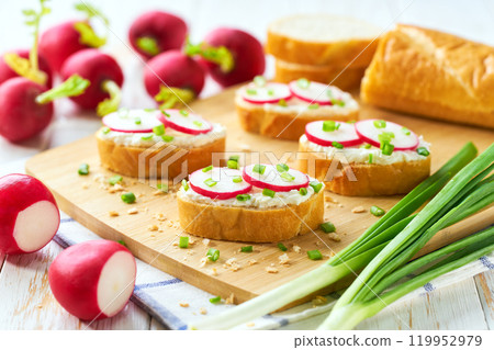 Cutting baguette with soft cream cheese and radish on a light kitchen table. Tasty summer snacks. Cutting baguette with soft cream cheese and radish on a light kitchen table. Tasty summer snacks. 119952979