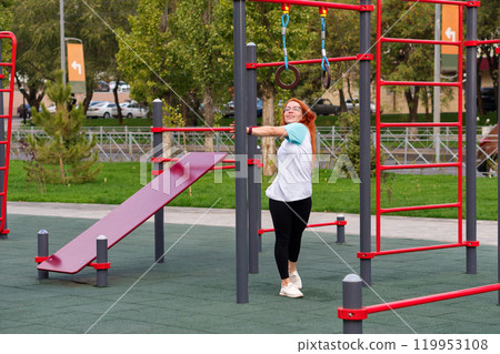 Woman on outdoor playground, smiling during exercise. 119953108