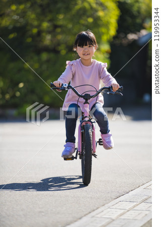 An elementary school girl trying to practice riding a bicycle 119953344