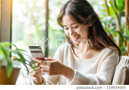Woman smiling while using smartphone in bright room with greenery Woman smiling while using smartphone in bright room with greenery 119954093