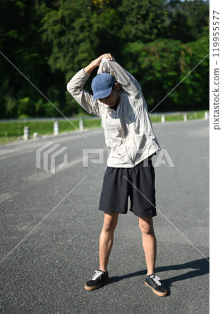 Full length man athlete warming up for an outdoor workout in a serene park Full length man athlete warming up for an outdoor workout in a serene park 119955577