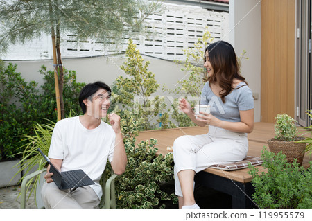 Happy young couple relaxing with technology and coffee in their backyard Happy young couple relaxing with technology and coffee in their backyard 119955579
