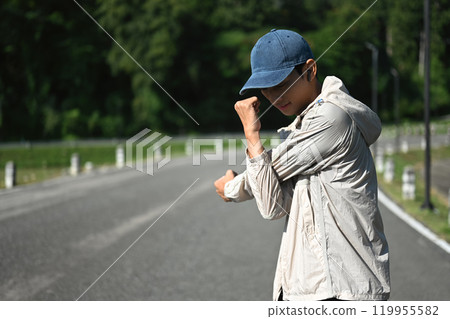 Young sportsman stretching his arms preparing for morning workout in the park 119955582