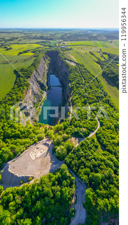The Velka Amerika Quarry in Czechia shines brightly under the sun, revealing its clear waters surrounded by lush greenery. This serene landscape invites nature lovers to explore its scenic beauty. The Velka Amerika Quarry in Czechia shines brightly under the sun, revealing its clear waters surrounded by lush greenery. This serene landscape invites nature lovers to explore its scenic beauty. 119956344