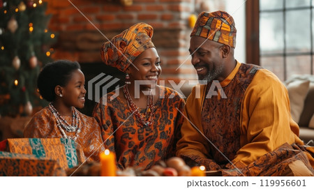 Smiling black family celebrating Kwanzaa together in traditional African clothing in warmly lit room 119956601