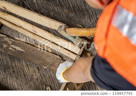 Workers in safety vest and glove using axe to work disassembling pallet parts 119957791