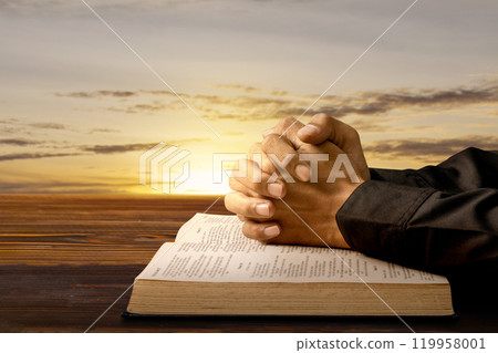Man praying with his hands on a opened holy bible on wooden table. Symbol of faith and worship in God Man praying with his hands on a opened holy bible on wooden table. Symbol of faith and worship in God 119958001