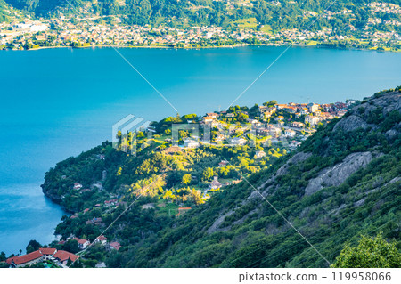 This serene landscape captures the stunning blue waters of Lake Como, framed by lush green hills and charming villas basking in the warm sunlight. A perfect summer day in Italy. 119958066