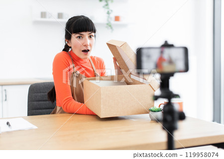 Caucasian female blogger surprised while unboxing during live streaming Caucasian female blogger surprised while unboxing during live streaming 119958074
