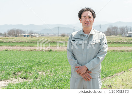 A middle-aged farmer man wearing work clothes standing in a rice field in the countryside A middle-aged farmer man wearing work clothes standing in a rice field in the countryside 119958273