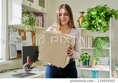 Young woman at home unpacks cardboard box with online purchases 119959565