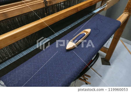 Traditional loom weaving with blue fabric and wooden shuttle for crafting and textile design Traditional loom weaving with blue fabric and wooden shuttle for crafting and textile design 119960053