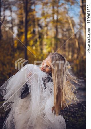 A woman in a white dress and leather jacket relaxes on a log in a vibrant forest during autumn A woman in a white dress and leather jacket relaxes on a log in a vibrant forest during autumn 119961891