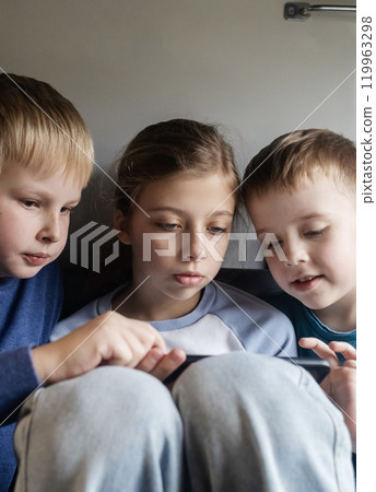 Children and the phone. Children's addiction to gadgets. Three children are traveling on a train and watching cartoons and playing games on a smartphone. 119963298