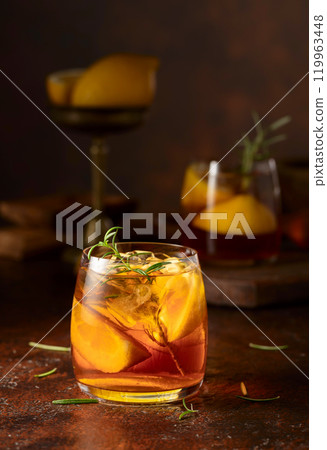 Iced tea or cocktail with ice, rosemary and lemon slices on the old brown table. 119963448