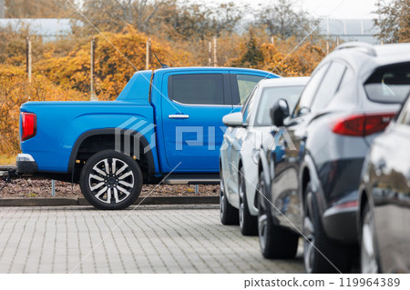 Side view of blue new ev pickup truck parked at outdoor parking lot automobile dealer or parking place against autumn foliage. Modern SUV electric vehicle outside Side view of blue new ev pickup truck parked at outdoor parking lot automobile dealer or parking place against autumn foliage. Modern SUV electric vehicle outside 119964389