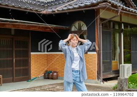 A woman holding her head in front of an old house, vacant house, countryside, inheritance A woman holding her head in front of an old house, vacant house, countryside, inheritance 119964702