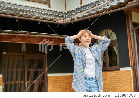 A woman holding her head in front of an old house, vacant house, countryside, inheritance A woman holding her head in front of an old house, vacant house, countryside, inheritance 119964708