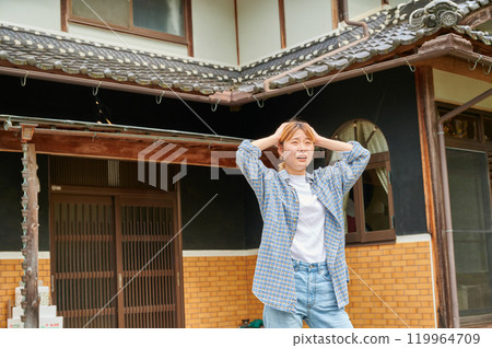A woman holding her head in front of an old house, vacant house, countryside, inheritance A woman holding her head in front of an old house, vacant house, countryside, inheritance 119964709