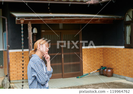 A woman tilts her head in front of an old house, vacant house, inheritance, countryside 119964762