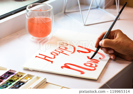 An artist drawing inscription Happy New Year with paints. A brush in female hand 119965314