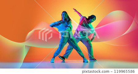 Creative design. Stylish man and woman dancing hip-hop in casual clothes on gradient background with abstract flowing elements. 119965586