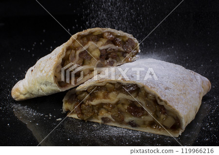 Apple strudel sprinkled with powdered sugar cut close-up on a black background Apple strudel sprinkled with powdered sugar cut close-up on a black background 119966216