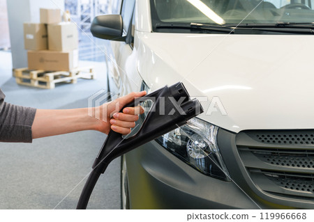 Hand with charging plug on a background of electric van. Concept. 119966668