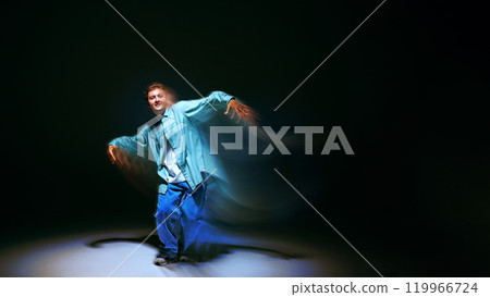 Creative design. Young man in casual clothes dancing contempt, freestyle, hip hop against black background with abstract light wave effect Creative design. Young man in casual clothes dancing contempt, freestyle, hip hop against black background with abstract light wave effect 119966724