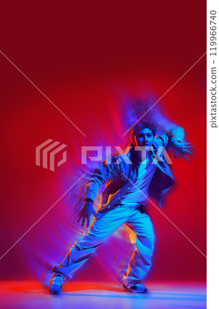 Creative design. Energetic performance of young man in casual clothes dancing hip hop, freestyle dance on red background with light wave effect Creative design. Energetic performance of young man in casual clothes dancing hip hop, freestyle dance on red background with light wave effect 119966740
