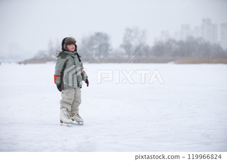 A little boy in huge skates is riding on the lake.Entertainment on a winter day for a child. A little boy in huge skates is riding on the lake.Entertainment on a winter day for a child. 119966824