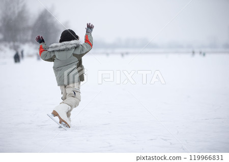A little boy in huge skates is riding on the lake A little boy in huge skates is riding on the lake 119966831