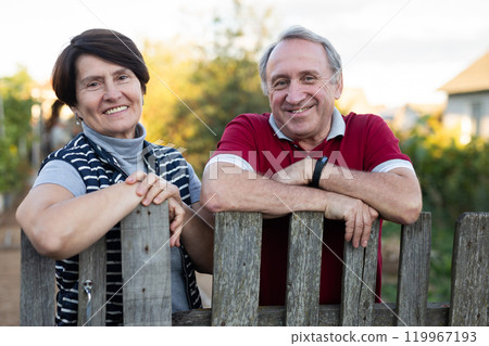 Positive mature man and woman standing near fence in garden Positive mature man and woman standing near fence in garden 119967193