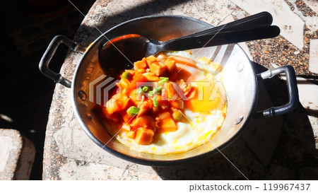 pan-fried egg with toppings, a breakfast of hot dog and fried egg in a small pan, shined by the warm morning sunlight 119967437