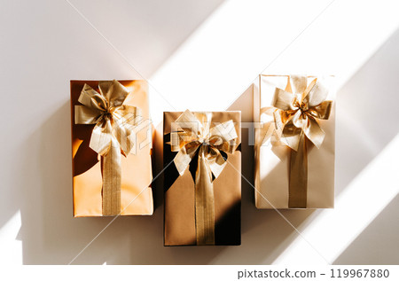 Three Christmas gift boxes, adorned with vibrant golden ribbons on white background with shadows 119967880