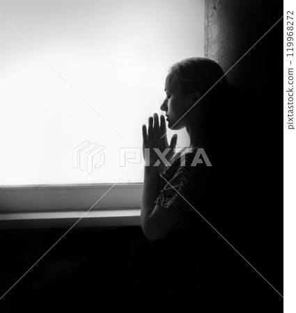 Young girl prays at the window 119968272