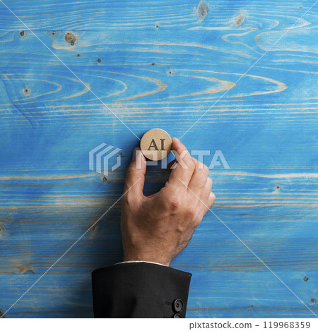 Hand of a businessman placing a wooden cut circle with an AI sign on it over textured blue background 119968359