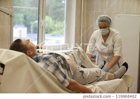 A nurse unidentified patient bandages a sore leg 119968482